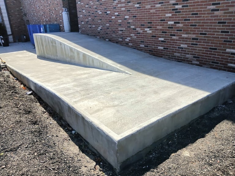 Concrete loading dock ramp against brick building with metal handrail on gravel ground