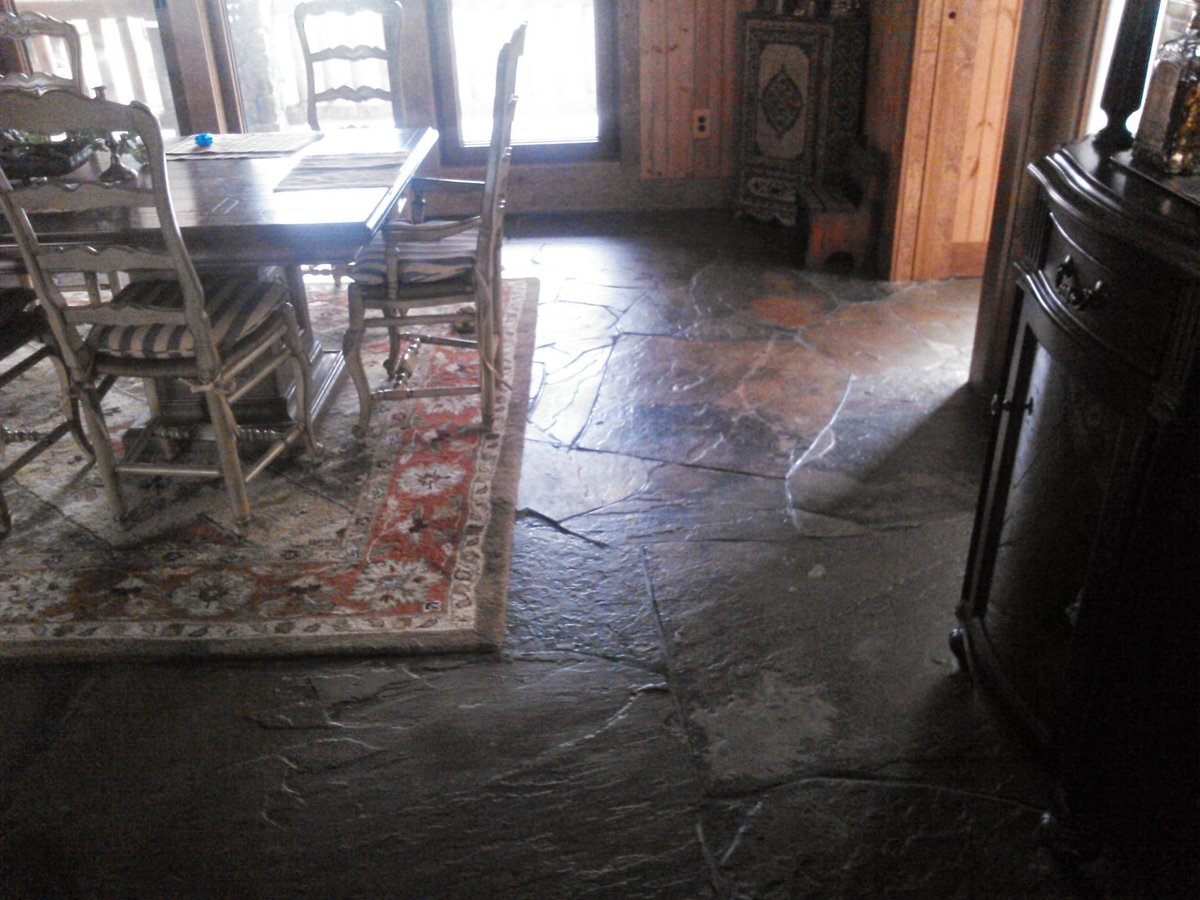 Interior room with stone floor, wooden chairs at table with rug, bright doorway, and dark furniture against walls