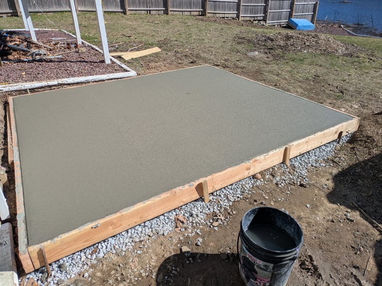 Freshly poured concrete pad with wooden frame in a backyard construction project