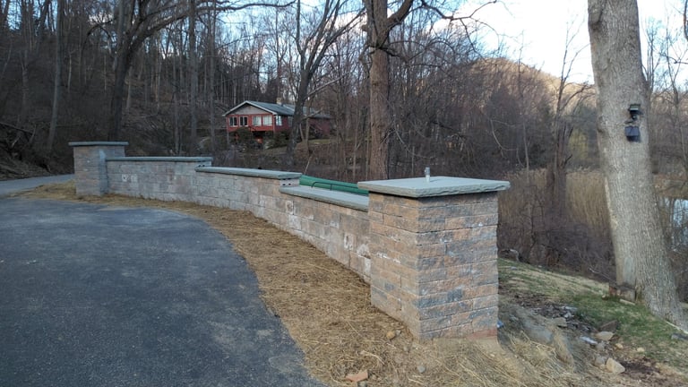 Stone wall and mailbox along a driveway with bare trees and a house in the background