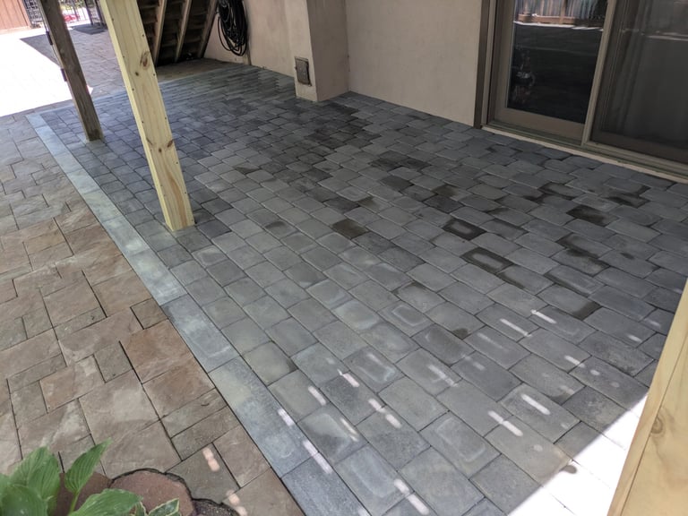 Empty covered patio or walkway with gray patterned pavers, wooden support columns, and white walls