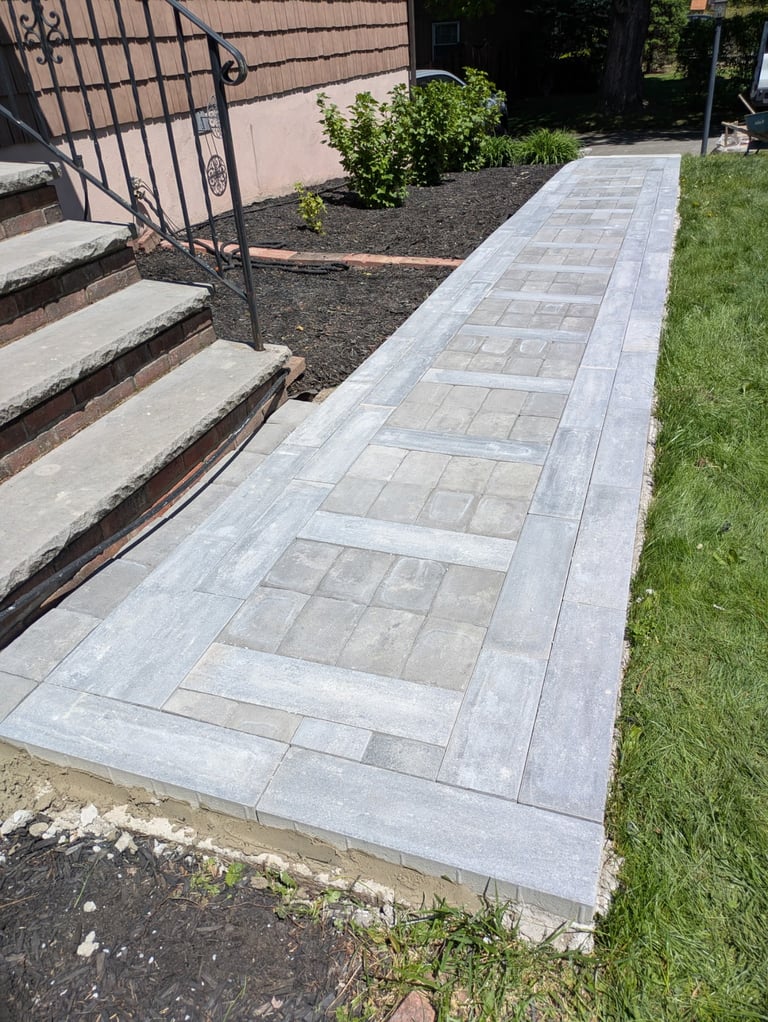 New gray paver walkway leading from ornate iron gate and brick steps to a grassy yard