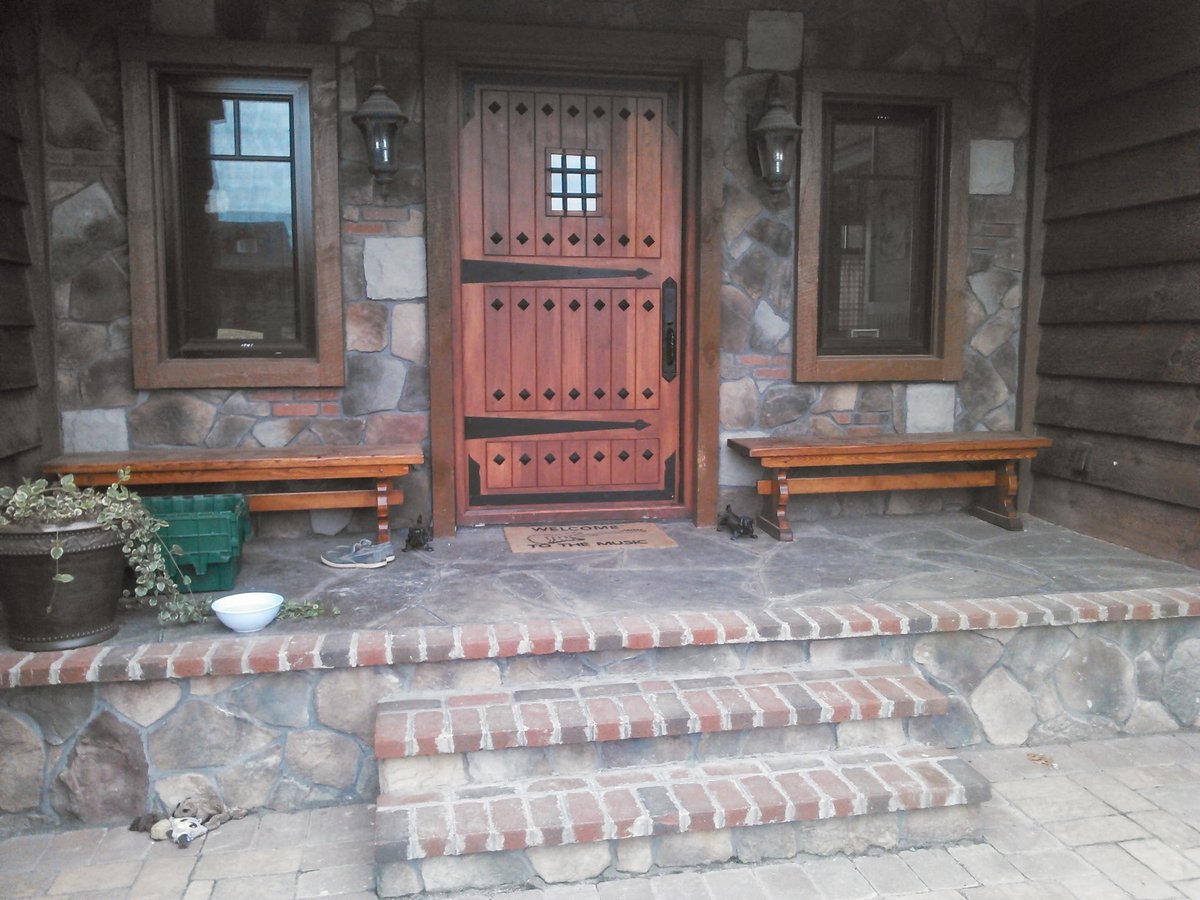 Stone entrance with red wooden double doors, brick steps, wooden benches, and side windows flanking the entryway