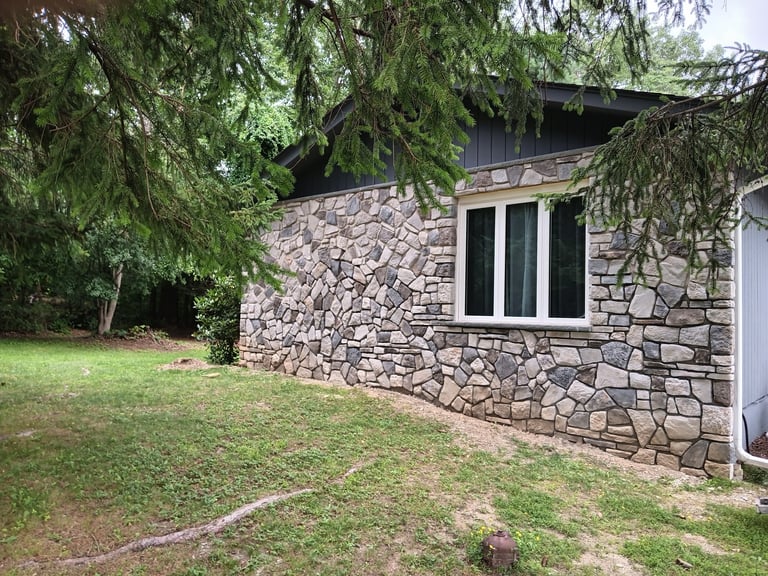Stone house exterior with large windows surrounded by grass lawn and overhanging tree branches